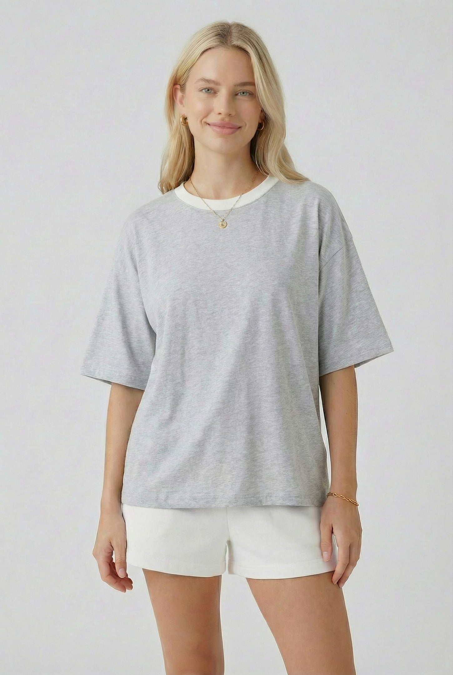 woman wearing a gray oversized t-shirt with a cream trim and white shorts, standing and smiling