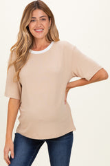 woman wearing a neutral beige maternity top with a white crew neckline and short sleeves, baby bump visible