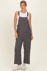 woman wearing a gray linen jumpsuit with adjustable straps and side pockets, paired with a white tank top and sneakers
