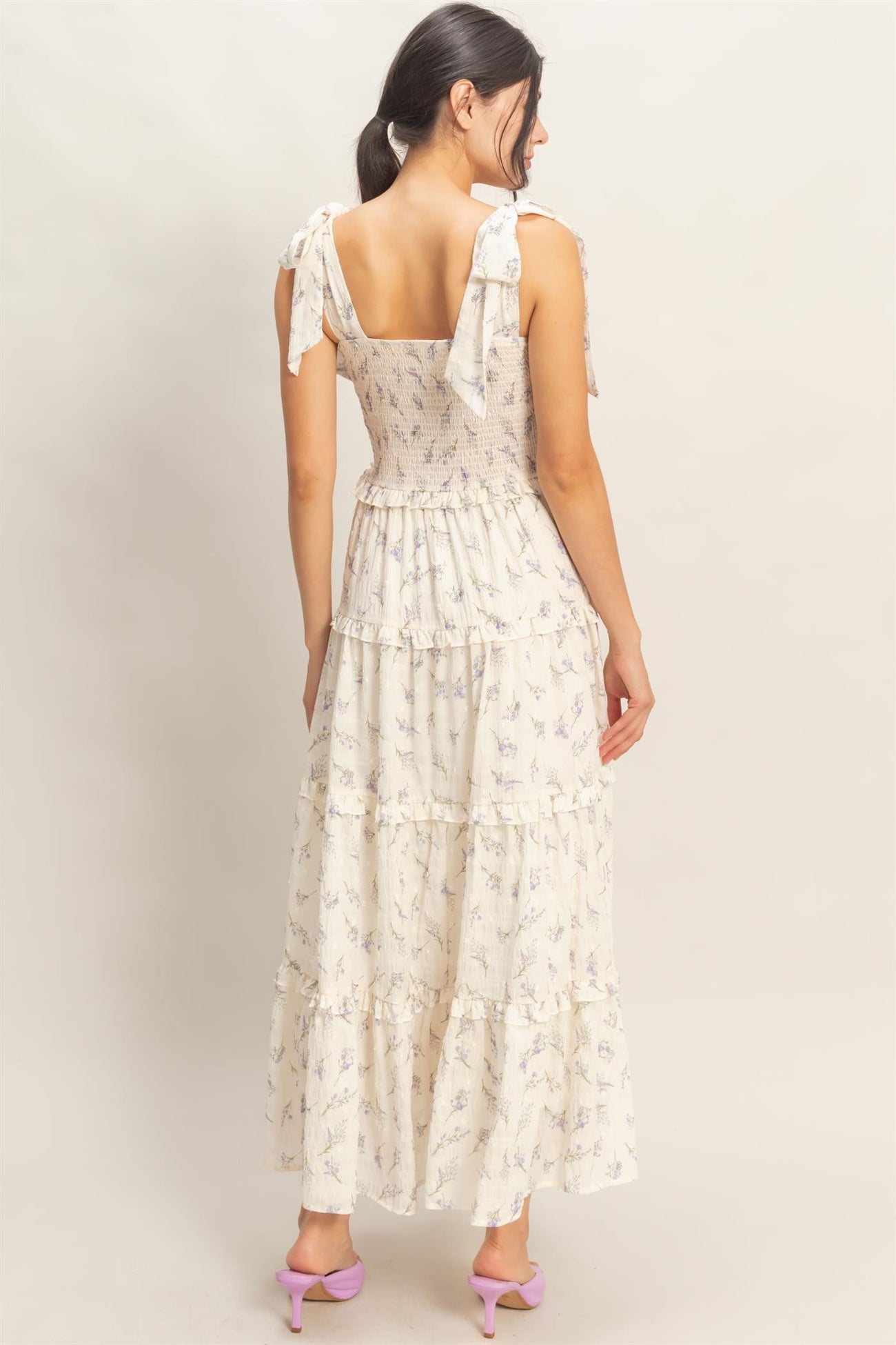 woman wearing a floral print maxi dress with tied shoulder straps and a tiered skirt, shown from the back