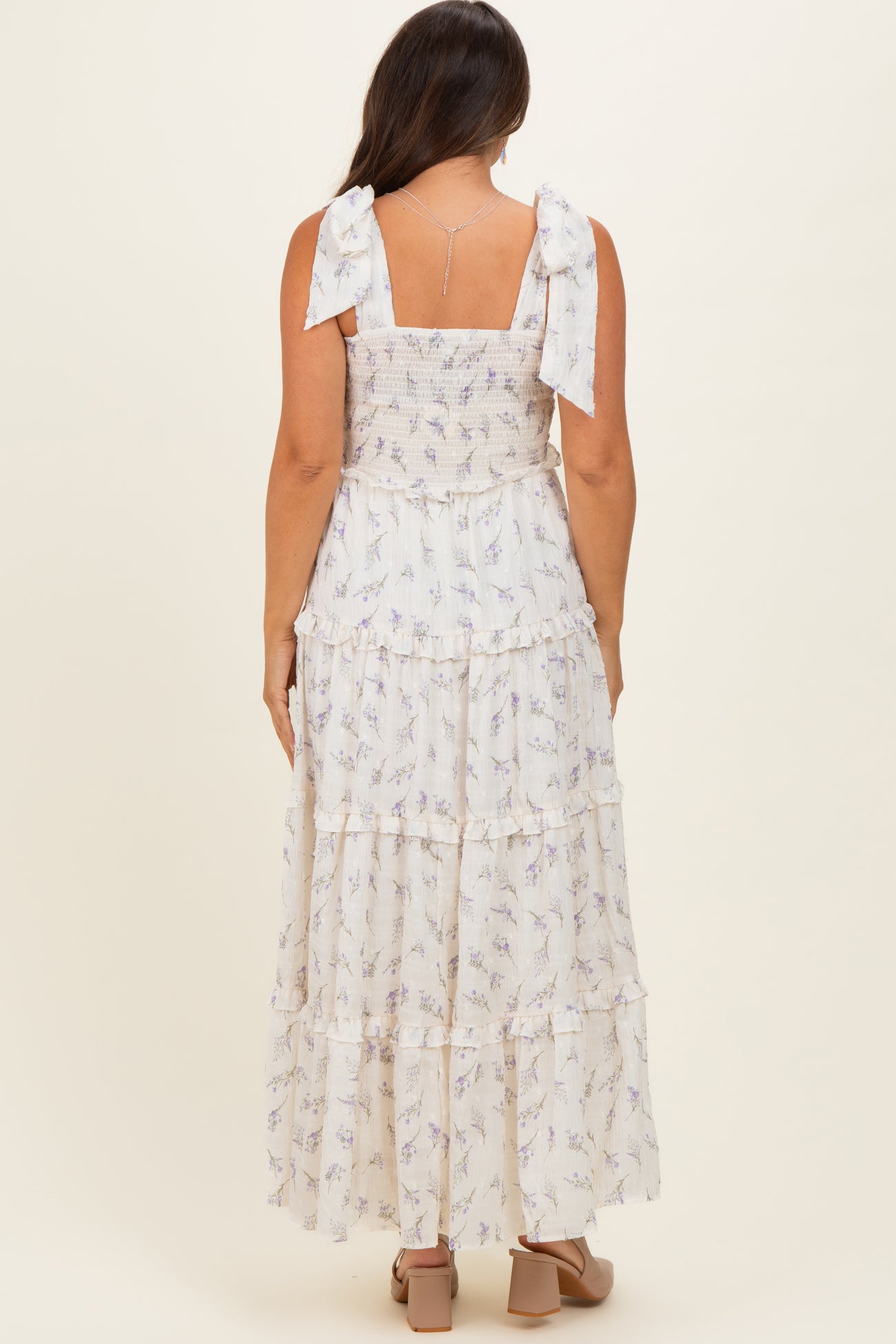 woman wearing a white floral maternity maxi dress with ruffled layers and bow straps, showing her pregnant belly