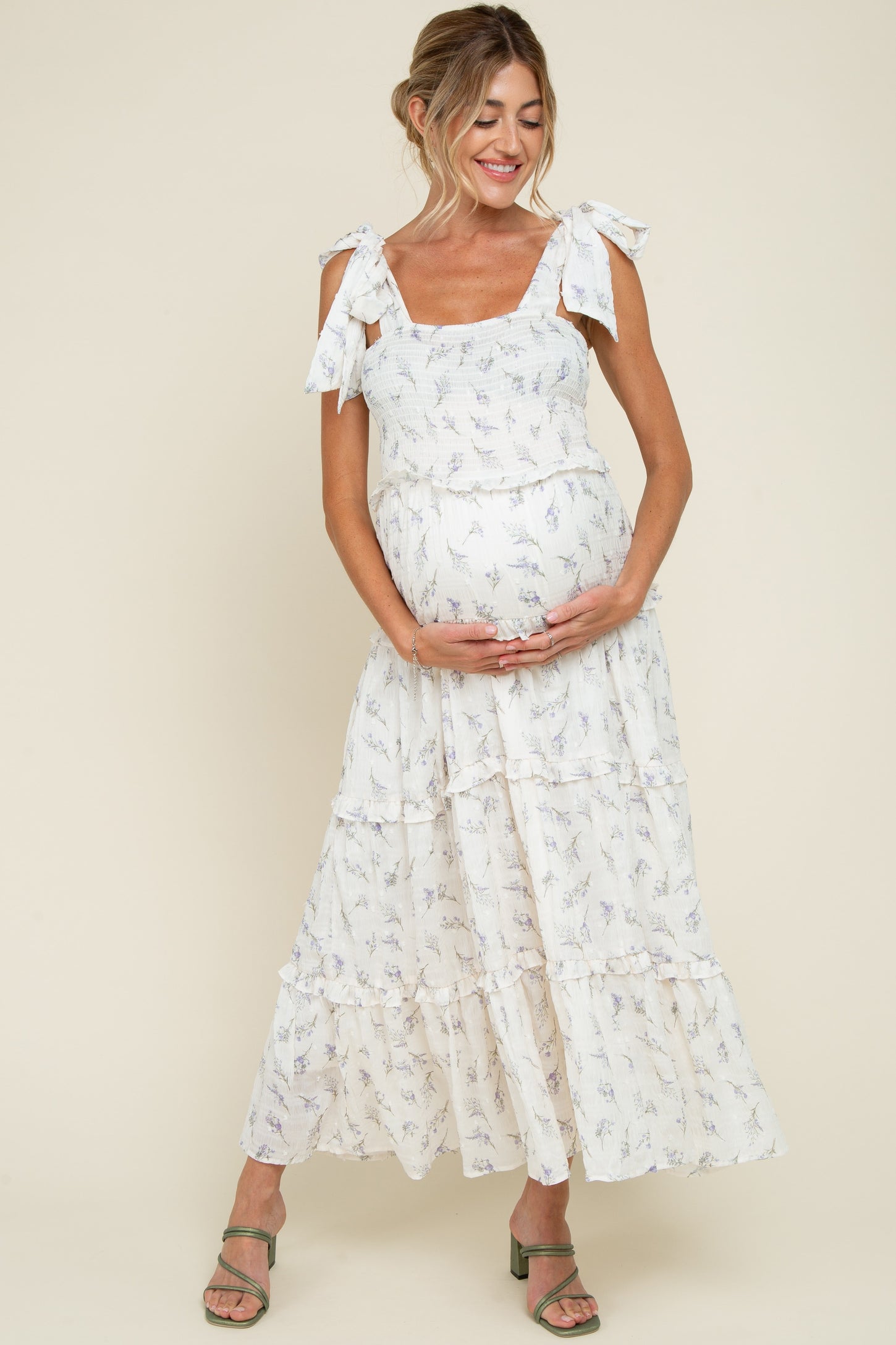 woman wearing a floral maternity maxi dress with bow straps, holding her baby bump and smiling