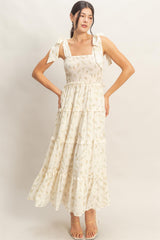woman wearing a light yellow floral maxi dress with tie straps and a tiered skirt