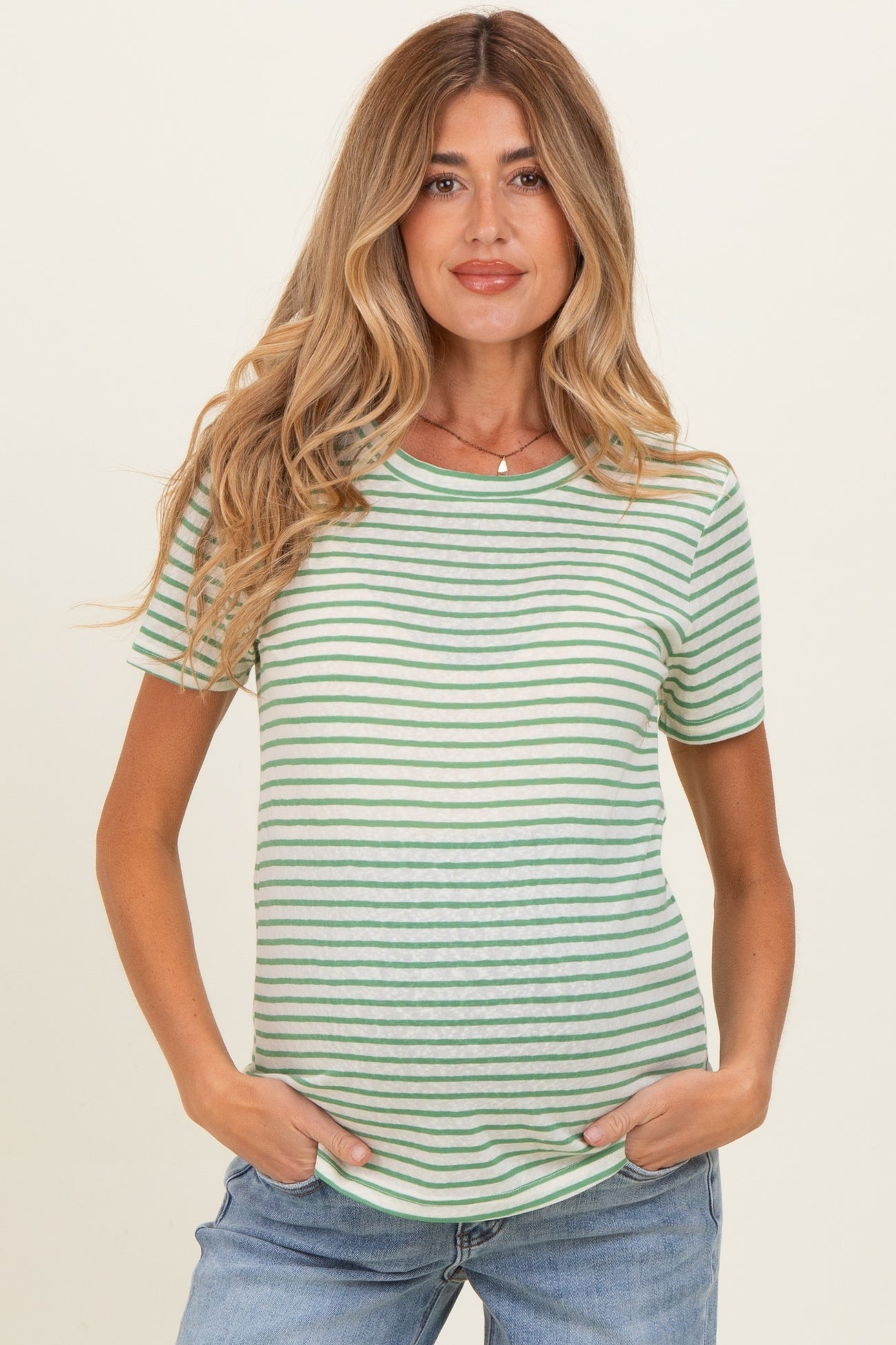 woman wearing a striped green maternity top with short sleeves and a baby bump, posing with hands in pockets