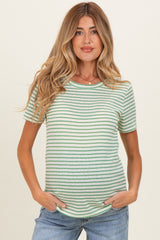 woman wearing a striped green maternity top with short sleeves and a baby bump, posing with hands in pockets