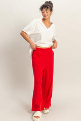 woman wearing a white v-neck t-shirt and red wide-leg pants, standing with hands in pockets