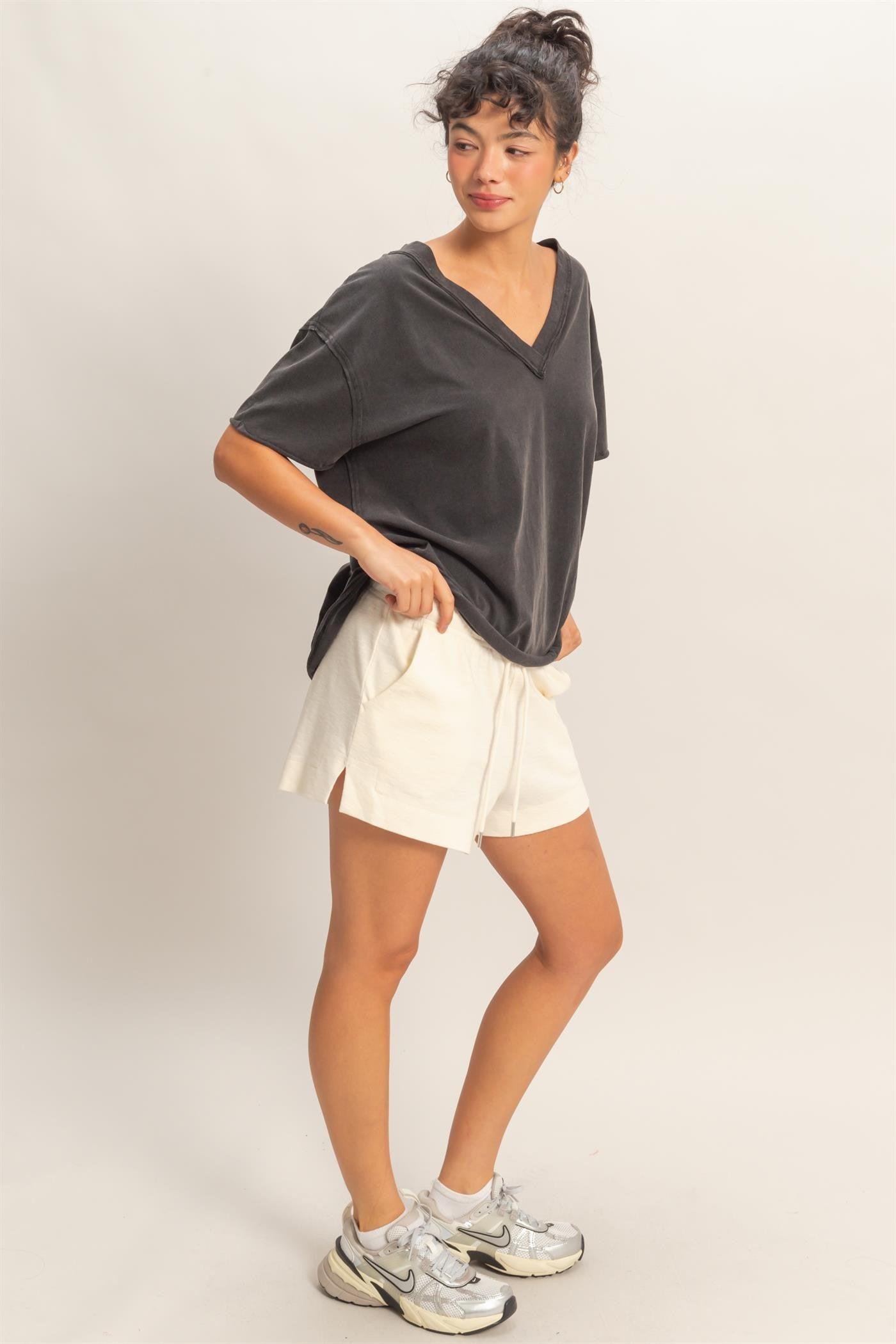 woman wearing a black oversized v-neck t-shirt and cream shorts, styled with silver sneakers
