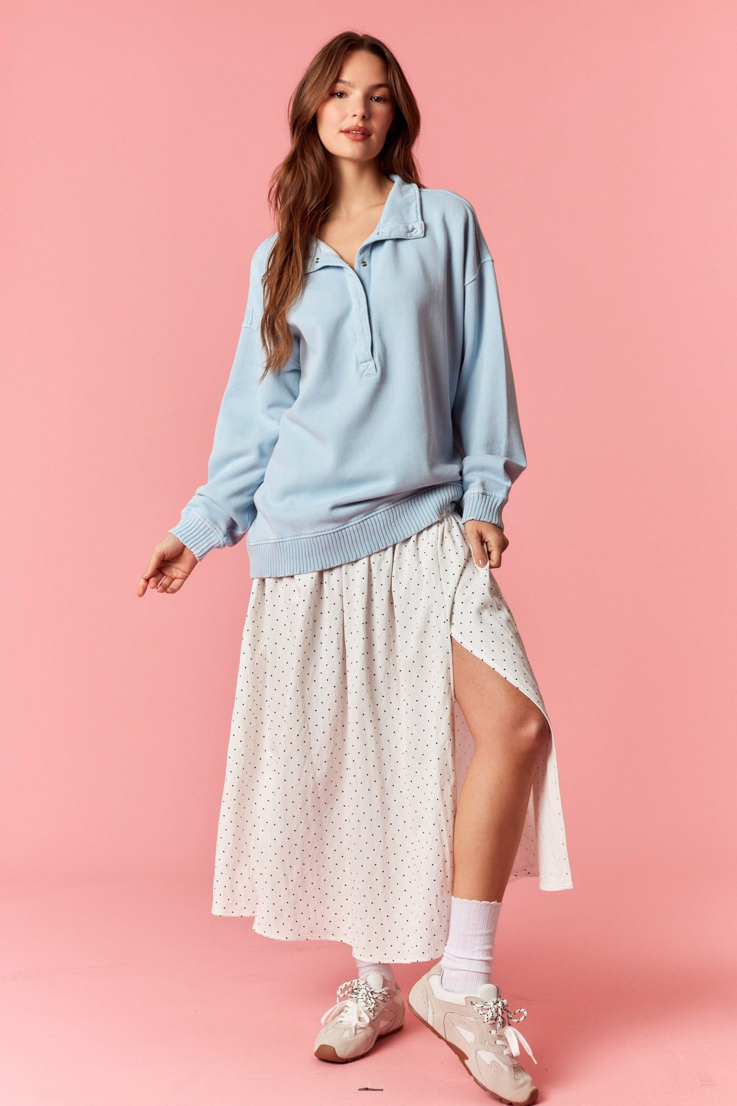 woman wearing a light blue oversized pullover and a white polka dot maxi skirt with a side slit and white sneakers
