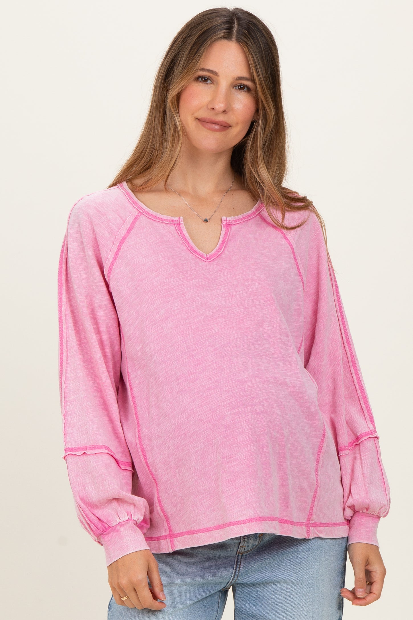 woman wearing a pink long sleeve maternity top with scoop neckline and contrast stitching, showing her baby bump