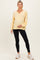 woman wearing a light yellow maternity sweatshirt and black leggings, with her baby bump gently visible
