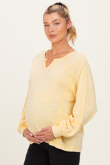 woman wearing a yellow maternity sweatshirt with a v-neck and balloon sleeves, gently cradling her baby bump