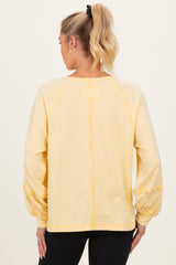 woman wearing a light yellow maternity top with balloon sleeves and a relaxed fit, seen from the back