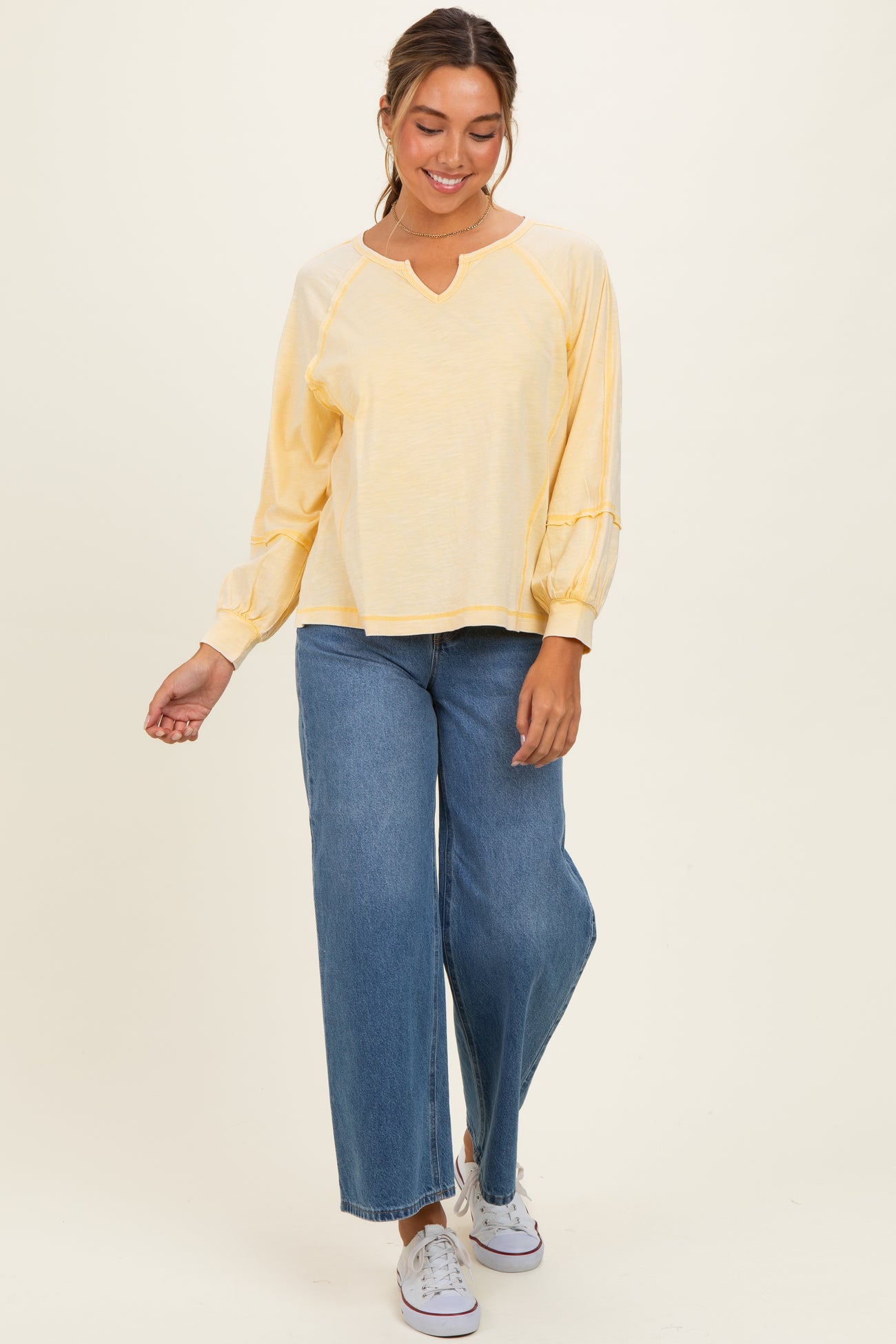 woman wearing a light yellow long sleeve top with a V-neck and wide-leg blue jeans