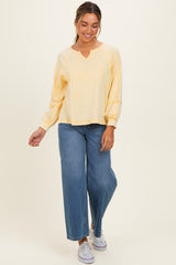 woman wearing a light yellow long sleeve top with a V-neck and wide-leg blue jeans