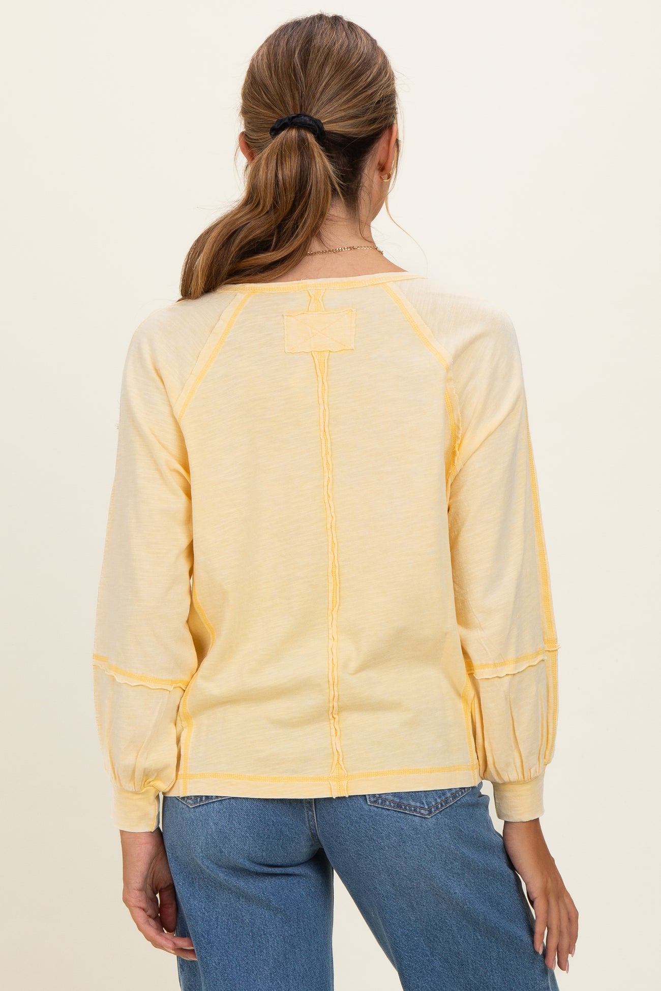 woman wearing a yellow long sleeve top with puffed sleeves and a relaxed fit, seen from the back
