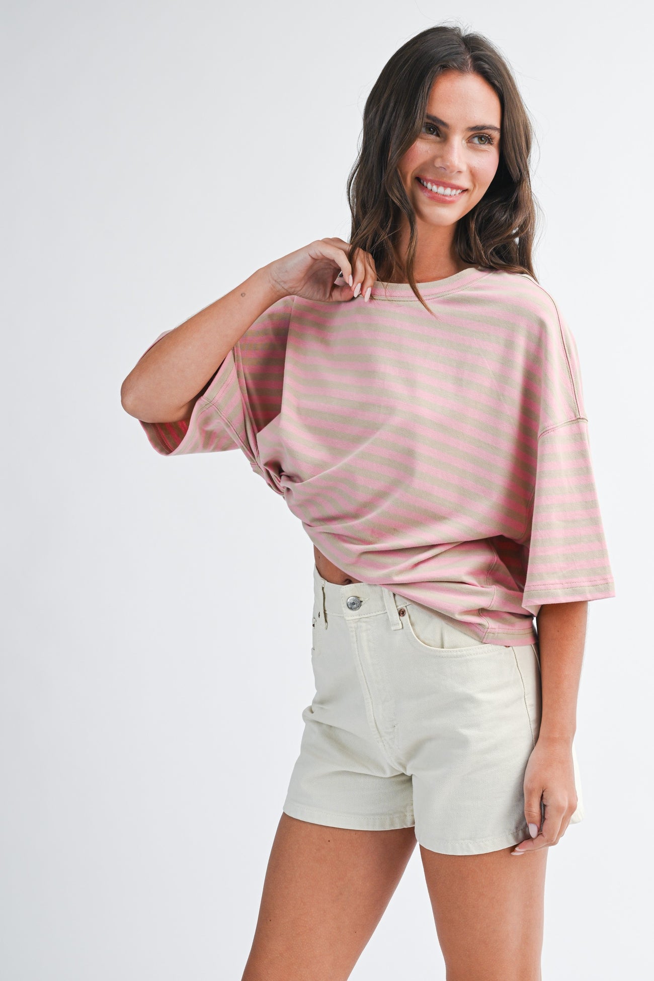 woman wearing a pink striped oversized t-shirt and light beige shorts with a casual pose