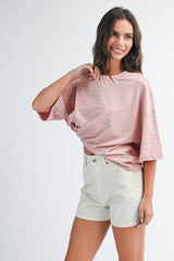 woman wearing a pink striped oversized t-shirt and light beige shorts with a casual pose