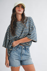 woman wearing a striped oversized t-shirt with rolled sleeves and denim shorts, accessorized with a light green cap