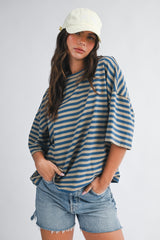 woman wearing a blue and beige striped oversized t-shirt with rolled sleeves and denim shorts, topped with a light yellow cap