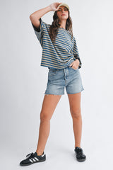 woman wearing a striped blue and green oversized t-shirt with denim shorts and black sneakers