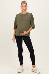 woman wearing an olive green oversized maternity top and black leggings, holding her baby bump