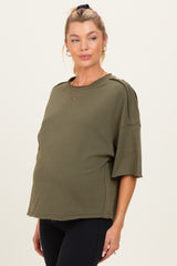 woman wearing an olive green maternity top with short sleeves and a relaxed fit, showing her baby bump