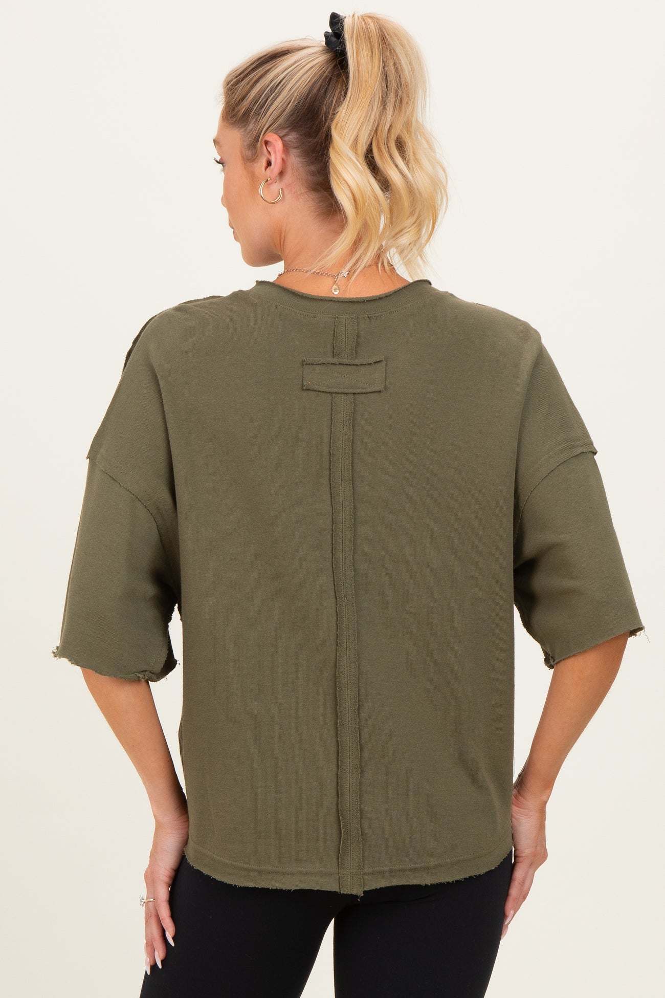 woman wearing an olive green maternity top with a relaxed fit and raw hem details, showcasing the back style