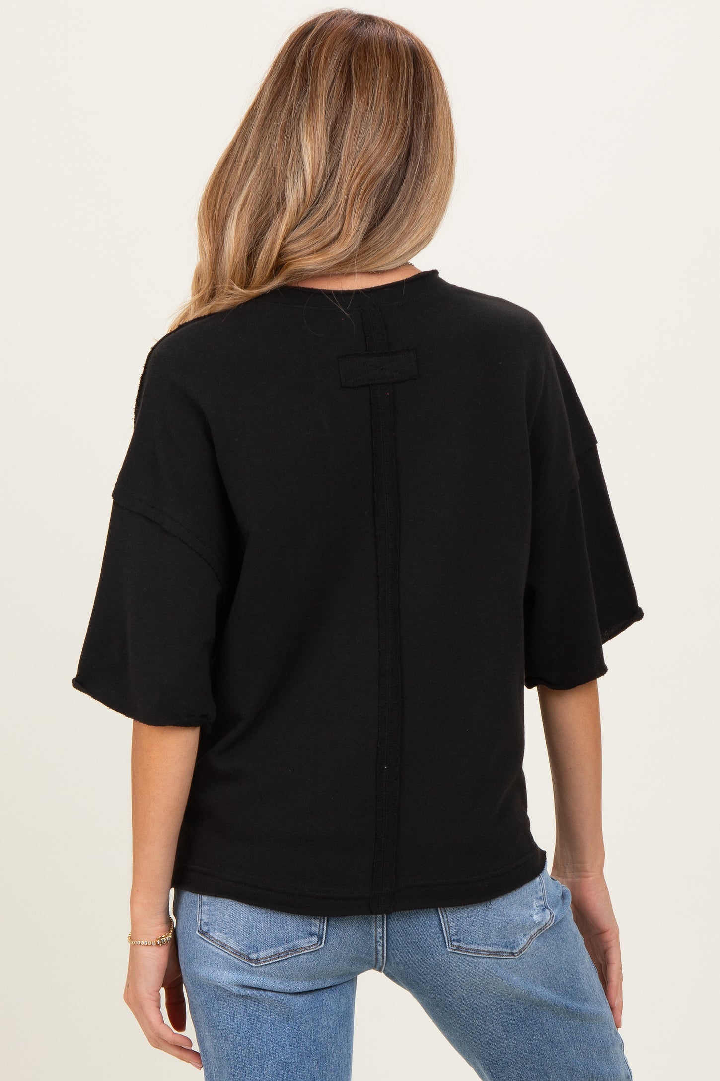 woman wearing a black oversized maternity sweatshirt with a back seam detail, paired with light blue jeans