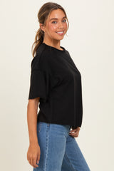 woman wearing a black oversized t-shirt paired with blue jeans, smiling while standing sideways