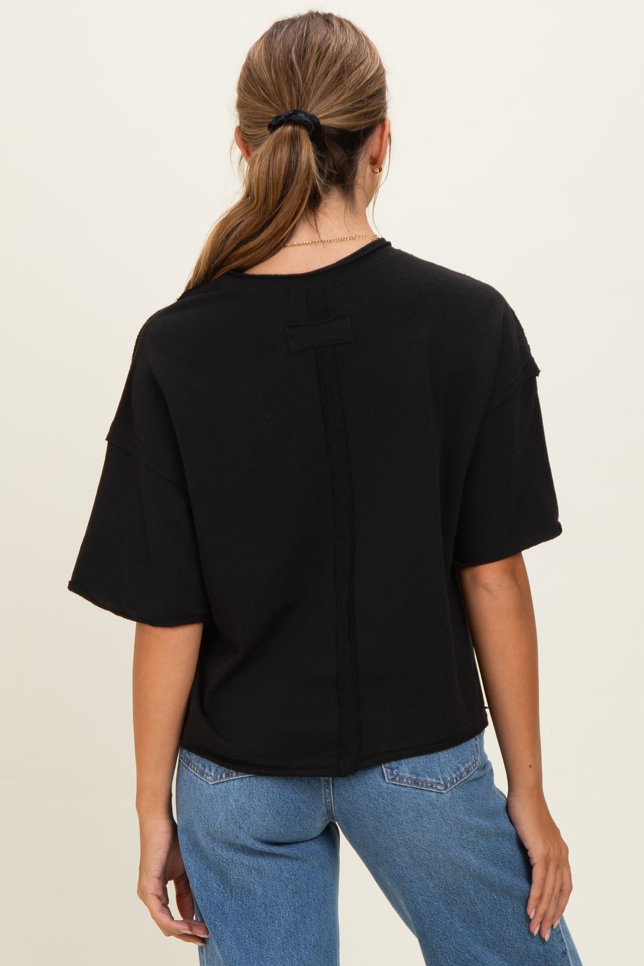 woman wearing a black oversized t-shirt with a minimalistic design and dropped shoulders, viewed from the back