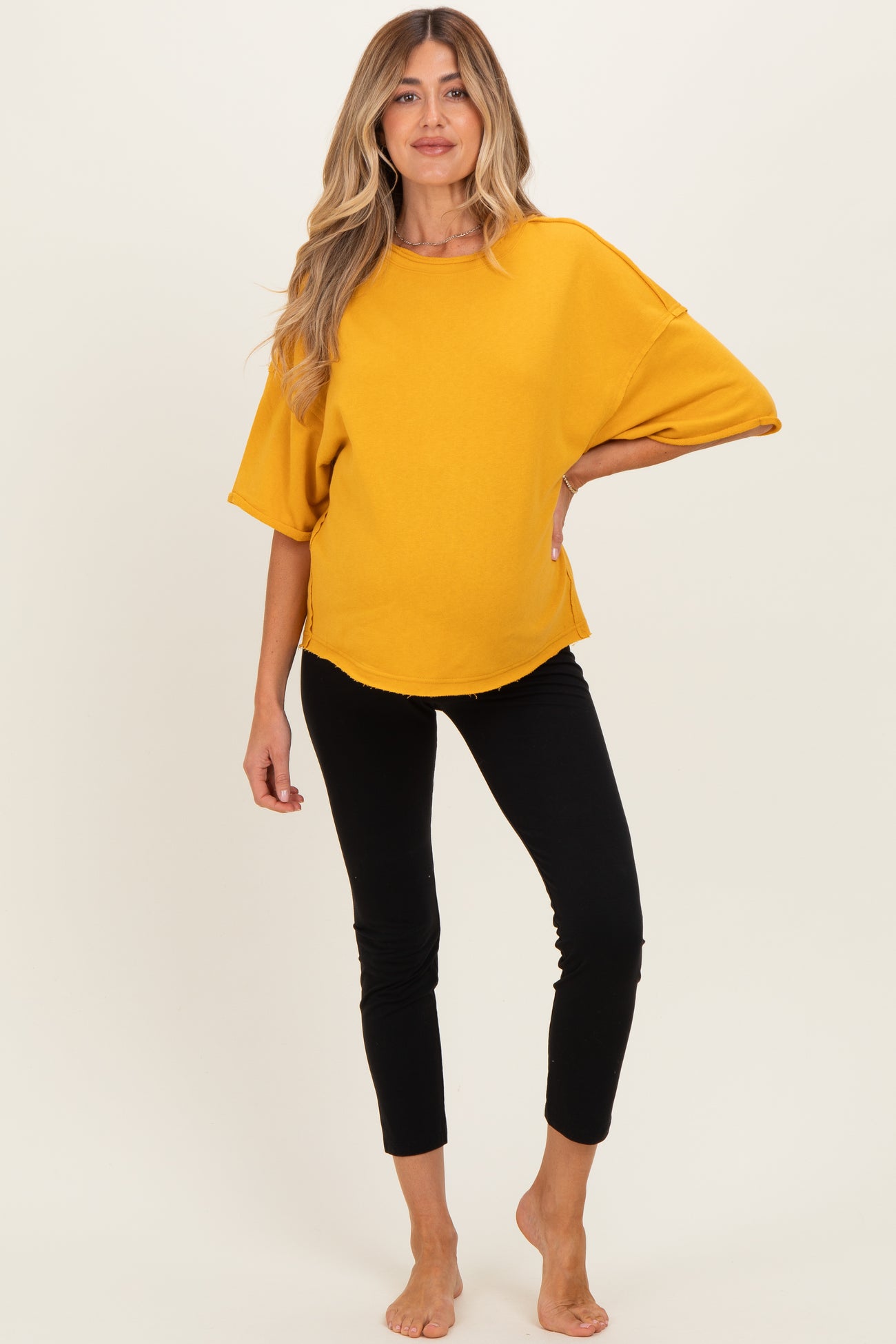 woman wearing a mustard yellow oversized maternity top and black leggings, showing her baby bump