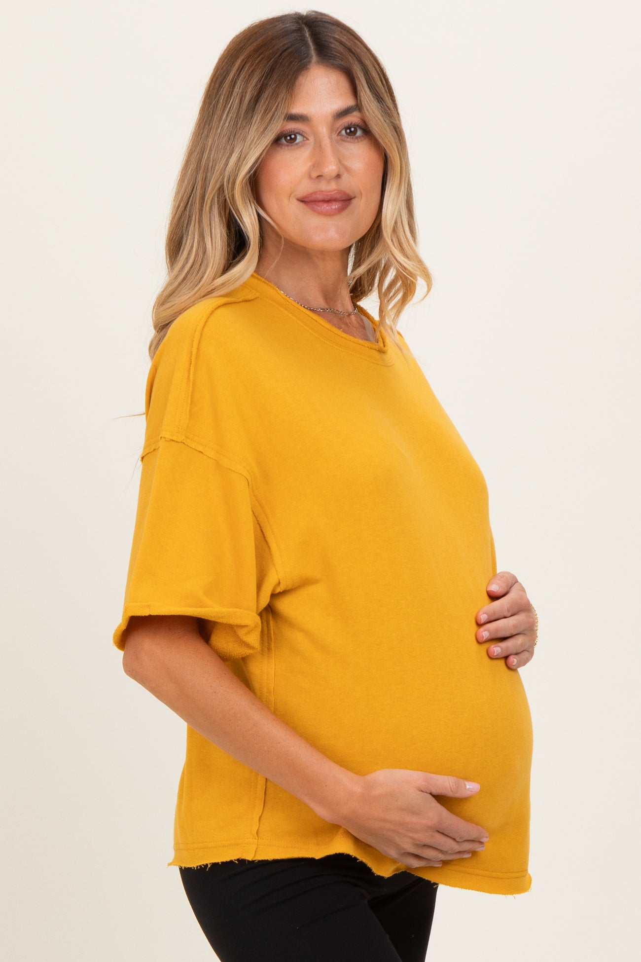 woman wearing a mustard yellow oversized maternity shirt and holding her baby bump