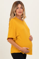 woman wearing a mustard yellow oversized maternity shirt and holding her baby bump