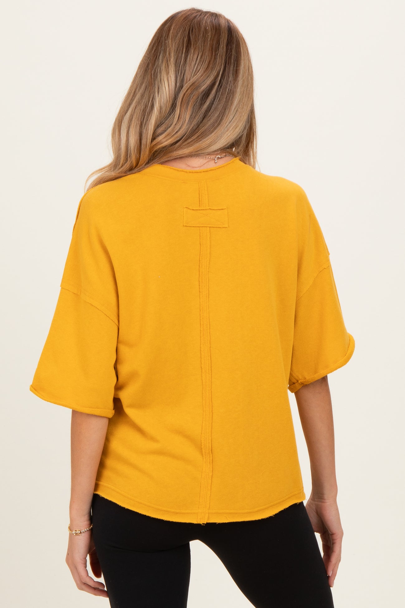 woman wearing a mustard yellow oversized maternity top with short sleeves and a back seam detail