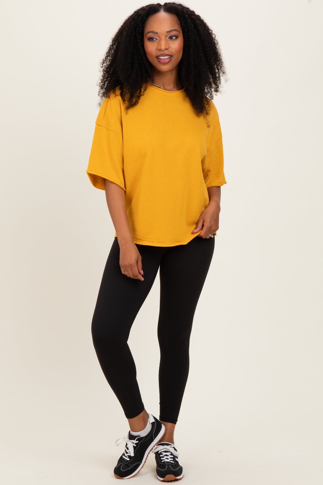 woman wearing an oversized mustard yellow t-shirt with black leggings and sneakers