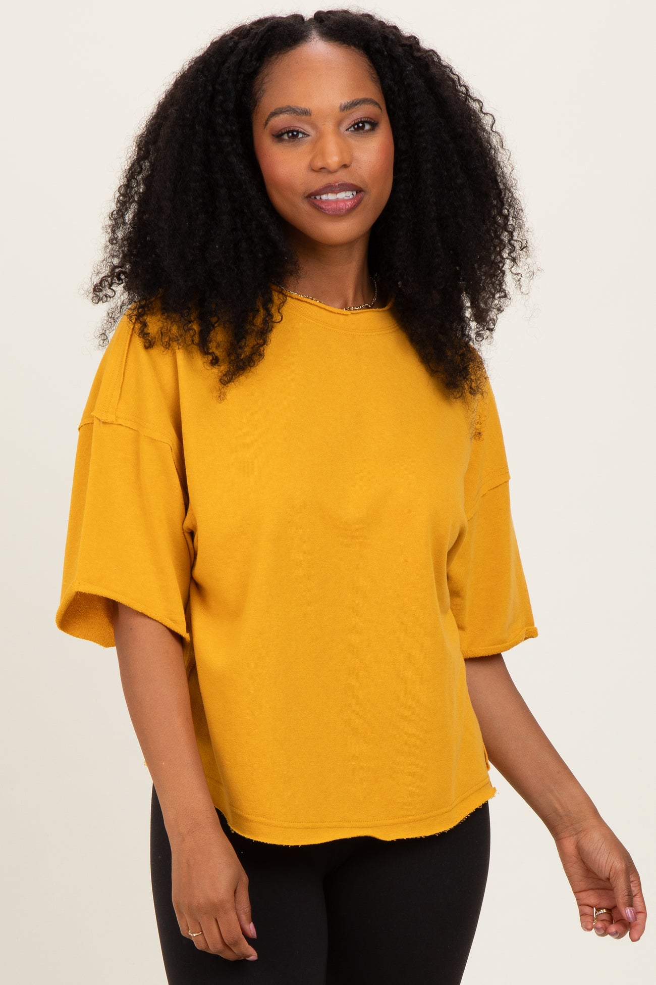 woman wearing a mustard yellow oversized t-shirt with short sleeves and a raw hem, posing confidently