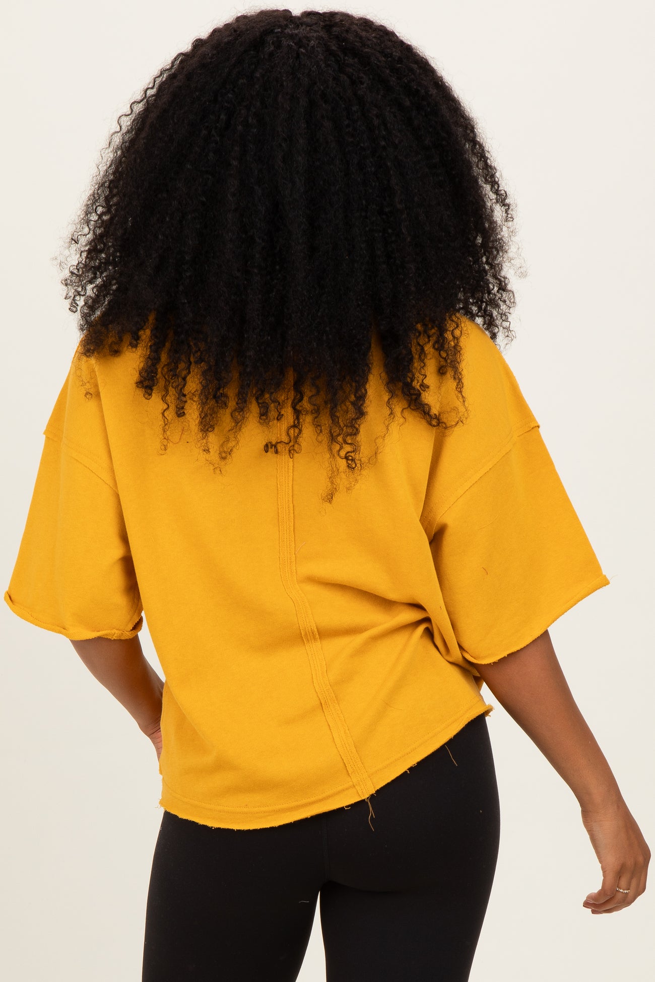 woman wearing a mustard yellow oversized tee with a raw hem and short sleeves, shown from the back