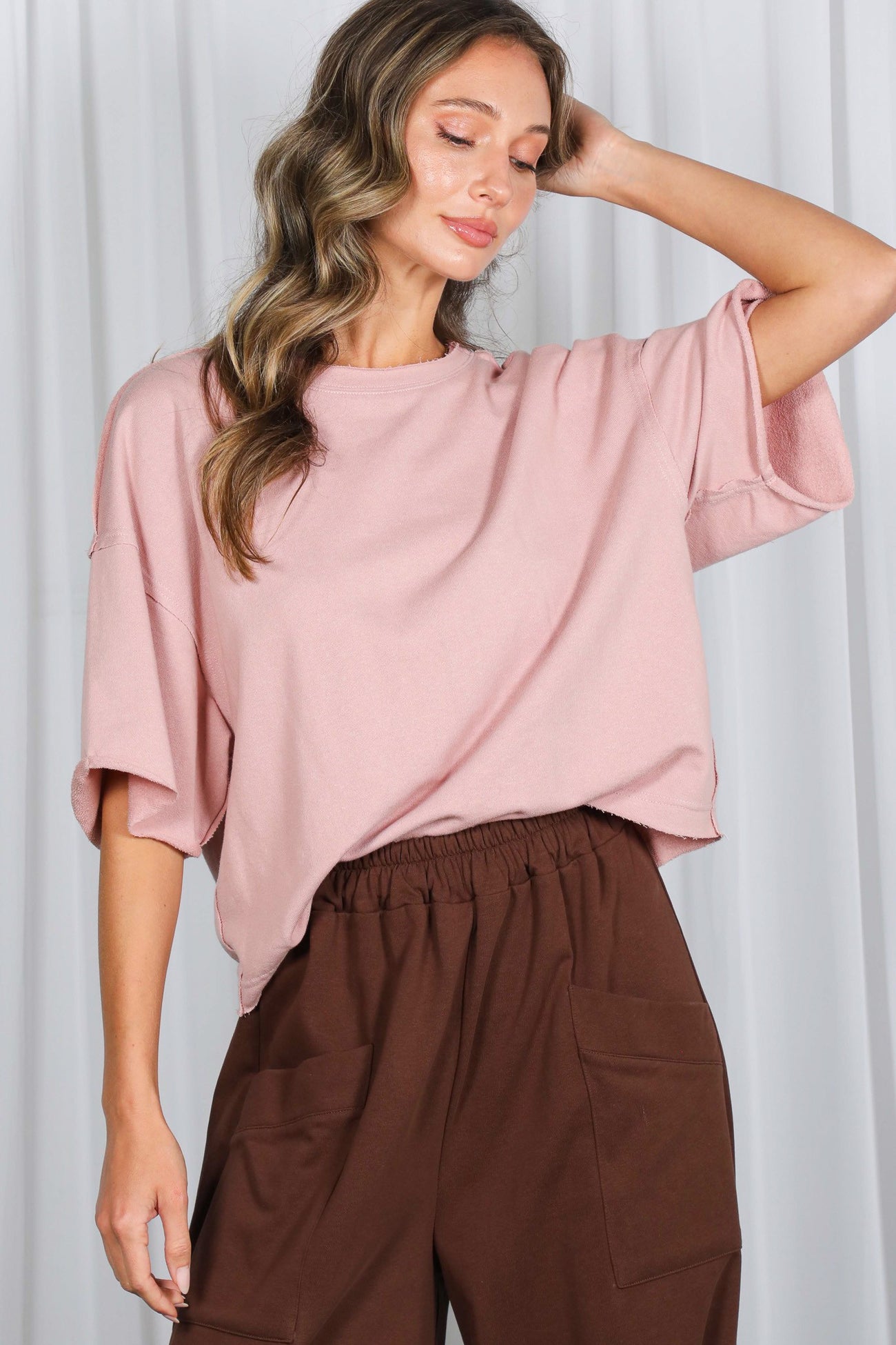 woman wearing a blush oversized short sleeve top with relaxed fit and brown high-waisted wide-leg pants