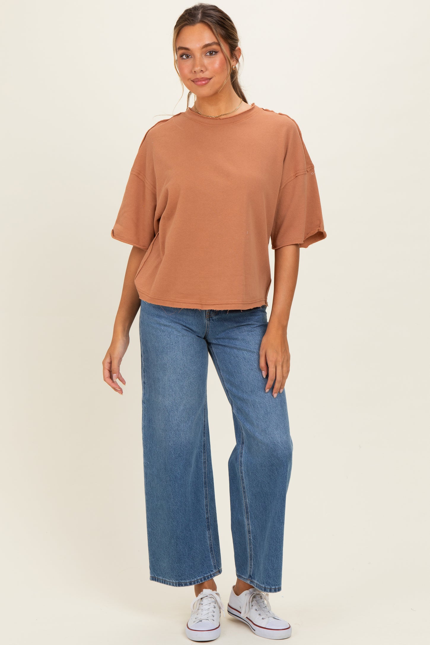 woman wearing a brown oversized short sleeve top with relaxed fit and light wash wide leg jeans