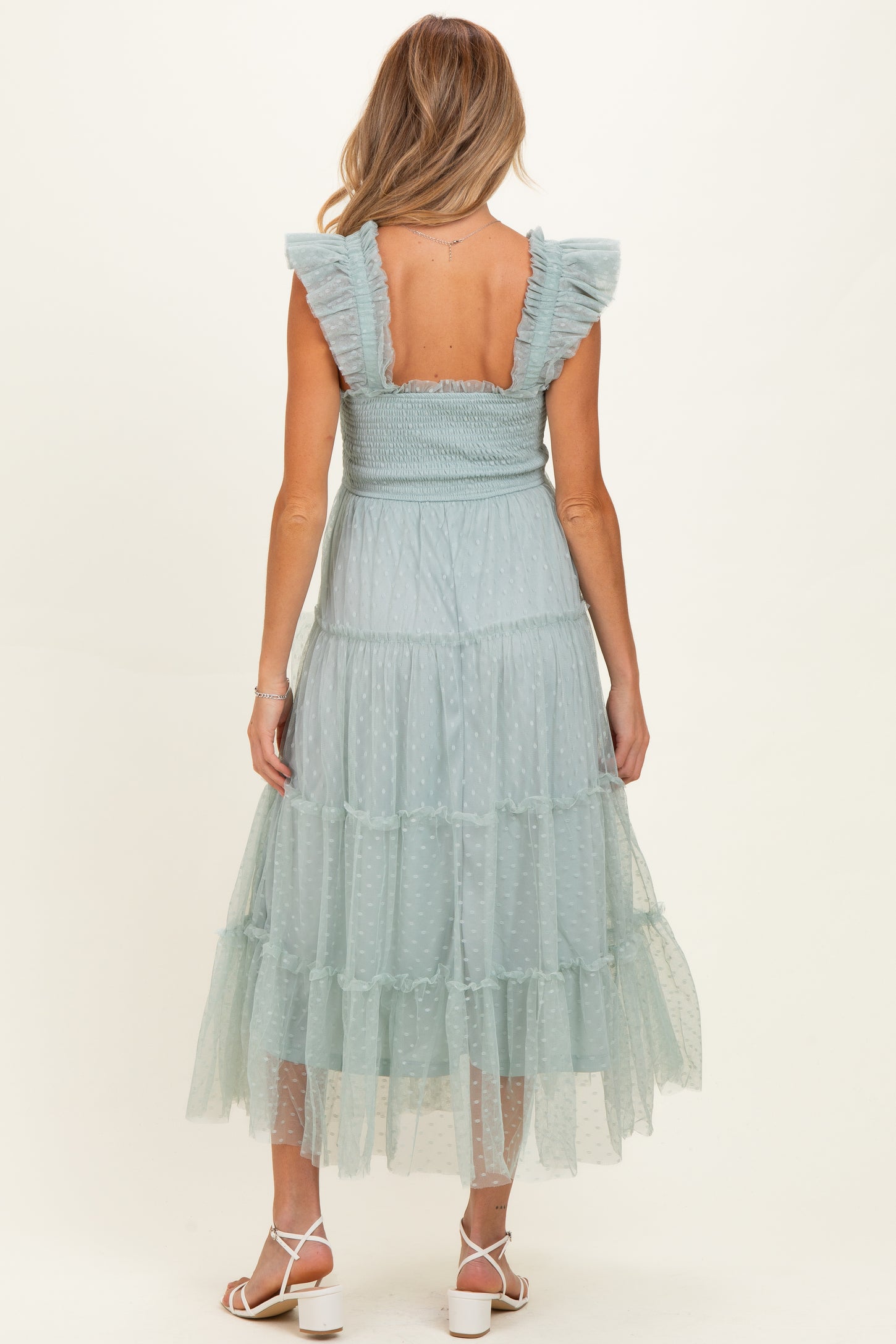 woman wearing a light blue maternity dress with ruffled sleeves and a tiered tulle skirt, showcasing her baby bump