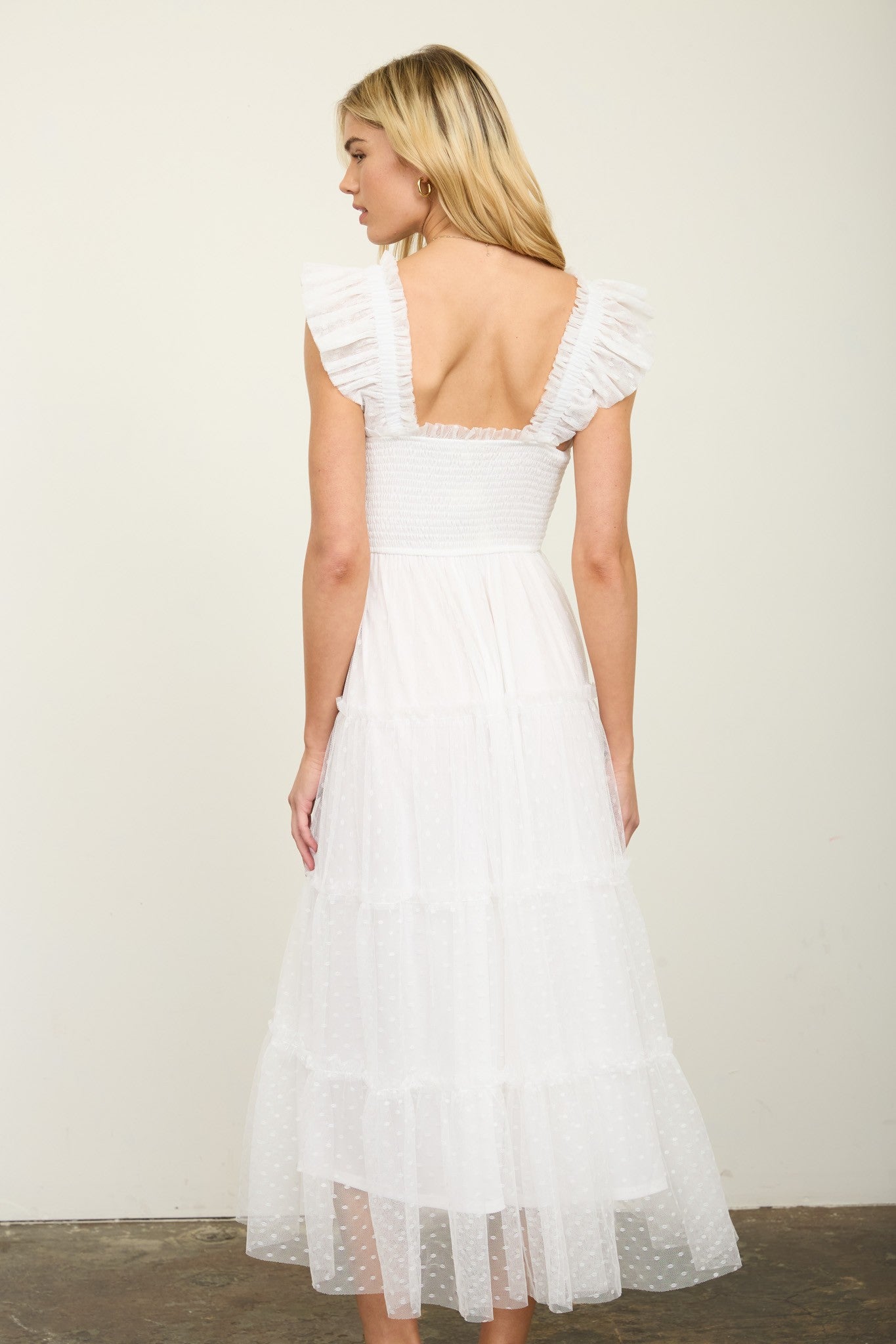 woman wearing a white tiered midi dress with ruffled sleeves and a smocked bodice, seen from the back