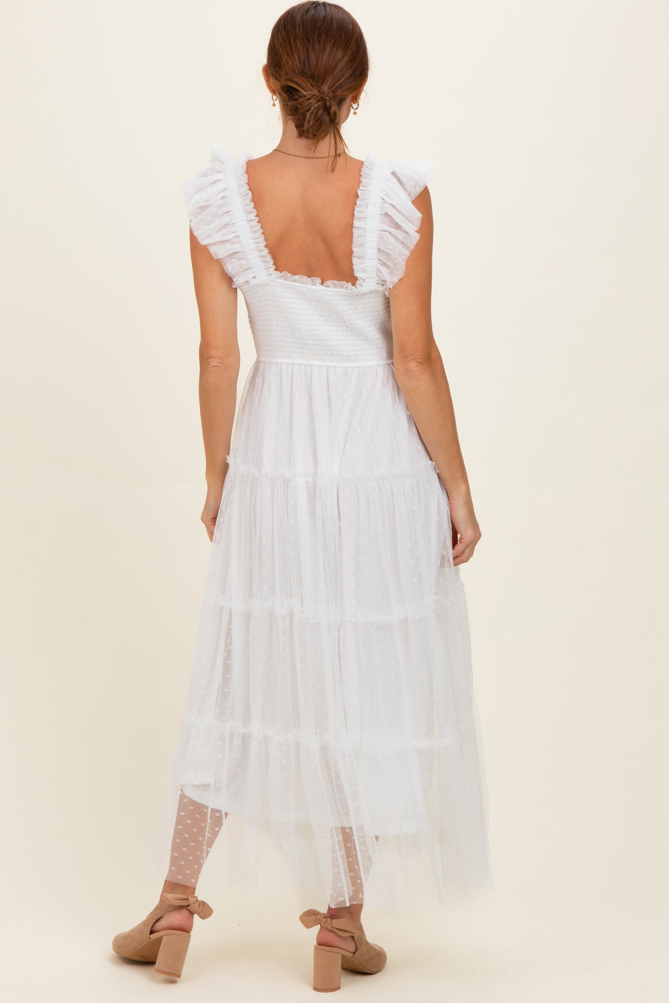 woman wearing a white tiered maxi dress with ruffle sleeves and a sheer overlay, seen from the back