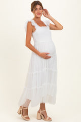 woman wearing a white maternity maxi dress with ruffled straps and a flowy tiered skirt, showing her baby bump