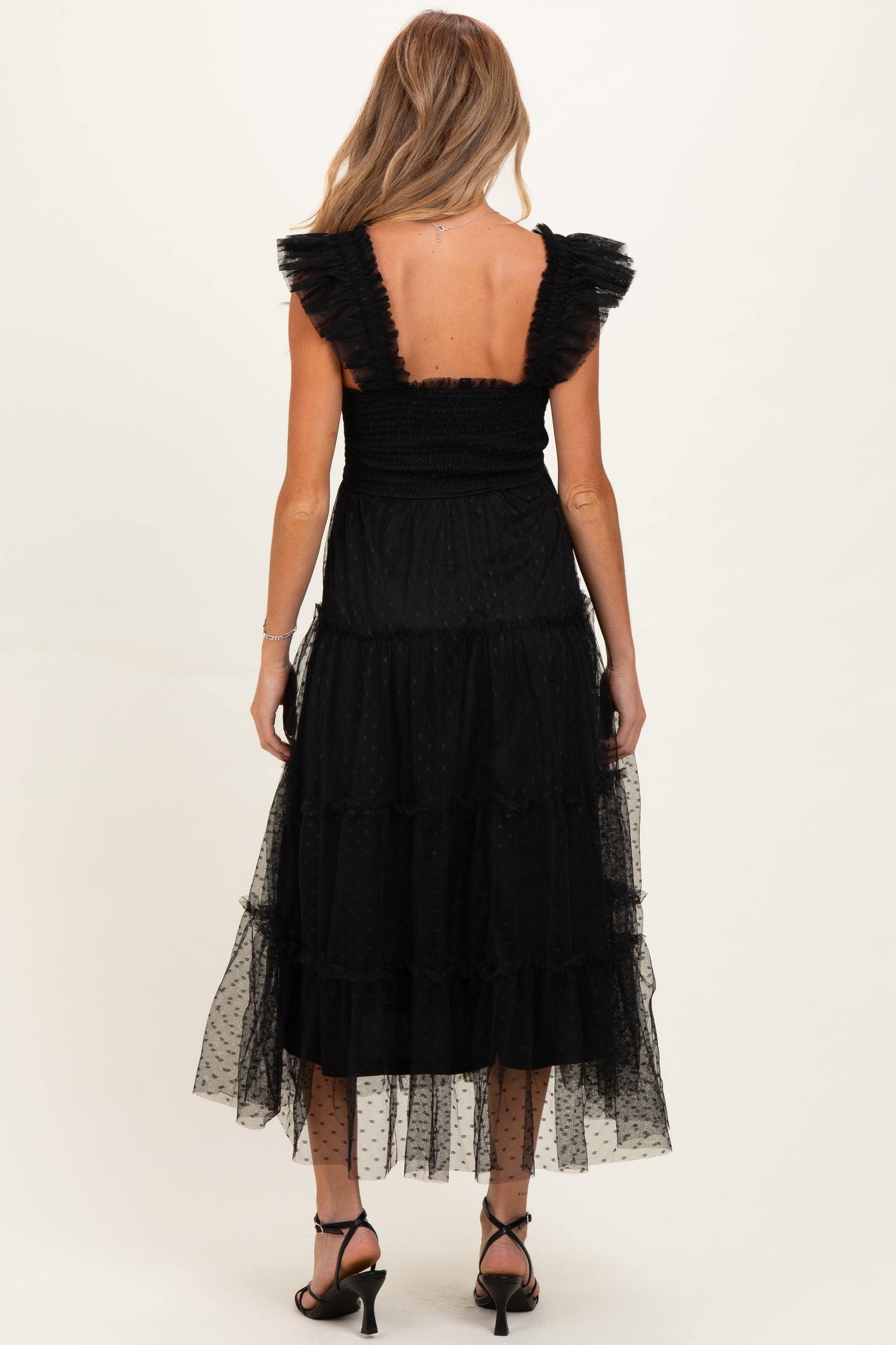 woman wearing a black tiered maternity dress with ruffled sleeves, showing a smocked back and sheer dotted fabric