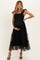 woman wearing a black maternity dress with ruffle straps and tiered tulle, gently holding her baby bump
