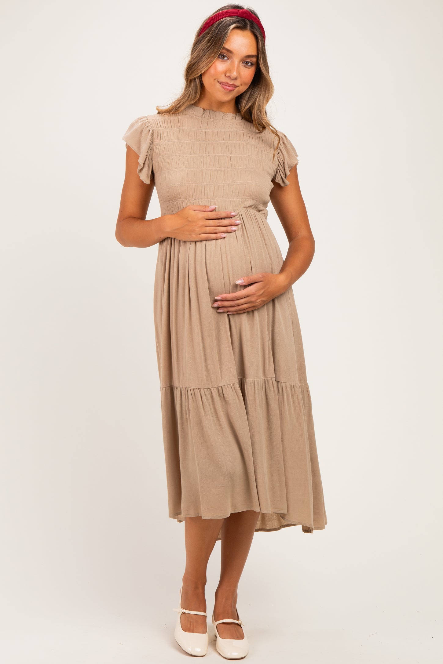 woman wearing a beige maternity dress with short puff sleeves and a smocked bodice, holding her baby bump