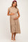 woman wearing a beige maternity dress with short puff sleeves and a smocked bodice, holding her baby bump
