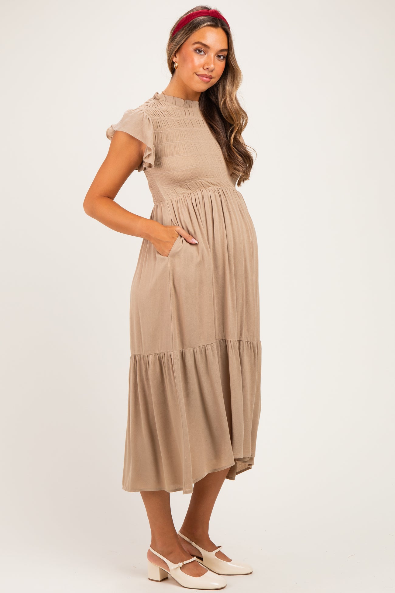woman wearing a beige maternity dress with short sleeves, smocked bodice, and a tiered skirt, showing her baby bump