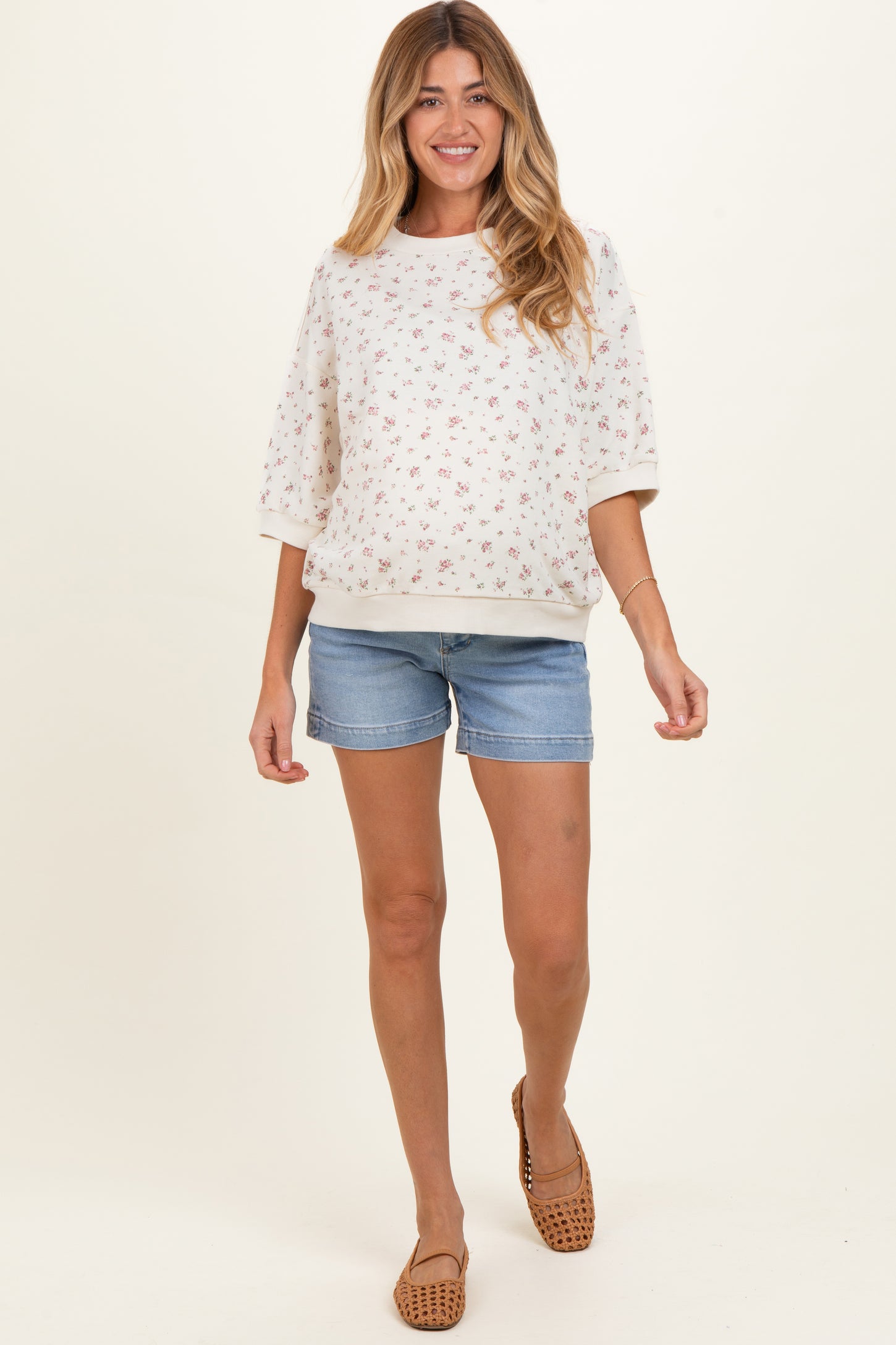 woman wearing a floral maternity sweatshirt with three-quarter sleeves and denim shorts