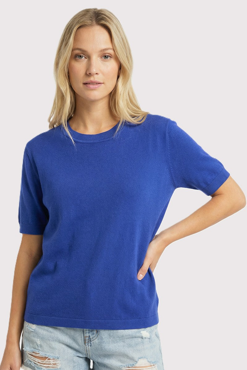 woman wearing a bright blue short sleeve sweater with a relaxed fit and slight texture, paired with distressed denim shorts
